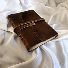 a brown leather book sitting on top of a white sheeted bed cover covered in wrinkle