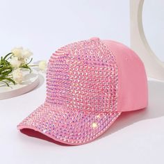 a pink hat with sequins on it next to a white vase and flowers