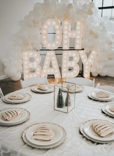 a white table topped with lots of plates and silverware next to a sign that says oh baby