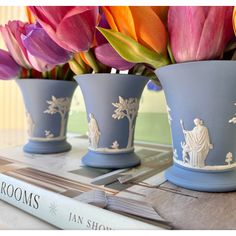 three blue vases with flowers in them sitting on a table next to a book