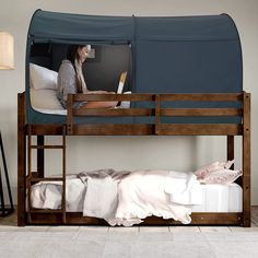 a woman sitting on top of a bunk bed next to a blue tent over her