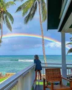 a woman standing on a balcony looking out at the ocean with a rainbow in the sky