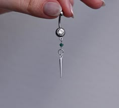 a person is holding onto a silver chain with a diamond and green bead hanging from it