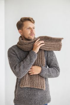 a man wearing a gray sweater and a brown knitted scarf is holding his hands on his chest