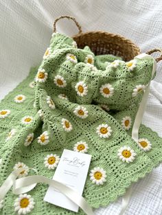 a green crocheted blanket with white daisies on it and a brown basket