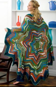 a woman is holding up a multicolored crocheted blanket in the shape of a star