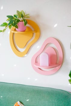 two planters are hanging on the wall next to a green couch with pink and yellow accents