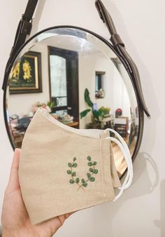 a person holding up a face mask in front of a mirror that is hanging on the wall