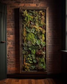 an art piece made out of moss and other plants in a frame on a brick wall