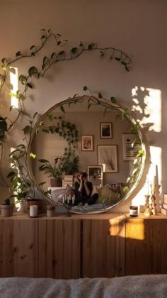 a mirror that is sitting on top of a dresser in front of a wall with plants