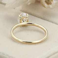 a gold ring with a diamond on it and some flowers in the back ground next to it