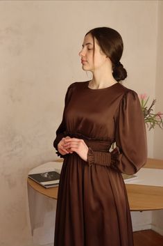 a woman standing in front of a table wearing a brown dress