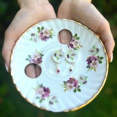 a person holding a white plate with pink flowers on it and two holes in the middle