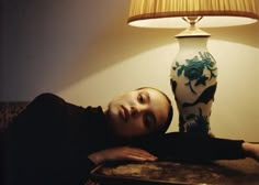 a woman laying on a couch next to a lamp with her head resting on the table