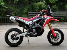 a red, white and blue motorcycle parked in front of a bench with trees behind it