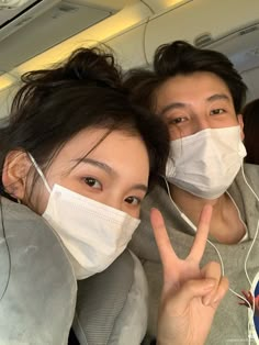 two people wearing face masks and making the peace sign with their hands while sitting on an airplane