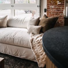 a white couch sitting in front of a window next to a brick wall and floor