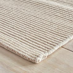 a close up view of a beige rug on a wooden floor, with the end of it