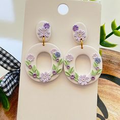 a pair of earrings with flowers on them sitting on top of a white card board