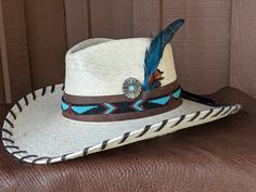 The Maverick starts with a Mexican soft palm leaf hat body that has a 3 3/4" brim and 5 1/4" crown. Hand laced in chocolate brown leather lace. The beaded hatband has a Thunderbird pattern and then mounted on distressed leather. The back of the band has a deer antler bead for accent. Starburst turquoise Concho and deep blue/green decorative feather completes the hat. All hats are made to order. Allow up to 4 weeks for your hat to ship. Brown High Crown Country Hat, High Crown Brown Country Hat, Western-styled Hat Band For High Crown Hats, Western Style Brown Panama Hat With Flat Crown, Brown High Crown Fedora For Country Events, Western Brown Panama Hat With Flat Crown, Brown High Crown Fedora For Western-themed Events, Rustic High Crown Hat For Rodeo, Custom Flat Brim Straw Hat For Rodeo