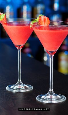 two martinis with strawberries sit on a bar top, ready to be served