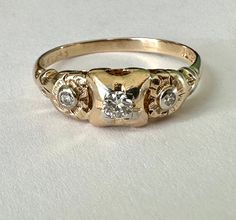 "a most wonderful vintage 14k gold ring with three diamonds, two flowers, and two golds.  this was intended as an engagement ring and likely made in the thirties or forties.  it had one chipped diamond which my jeweler did a beautiful job of replacing and it's looking pretty great for its age.  the central diamond is quite bright and is framed in a bit of white gold, as are the smaller ones.  i LOVE the flower designs around the smaller stones.  ring is marked Fidelity for the maker and 14k with Vintage 14k Gold Three-stone Rings, Vintage 14k Gold Three Stone Rings, Art Nouveau Wedding Ring, Ring With Three Diamonds, Engagement Rings Three, Random Numbers, Diamond Trilogy Ring, Art Nouveau Weddings, Vintage Gold Engagement Rings