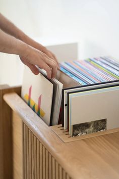 a person holding several books on top of a wooden shelf next to a book case