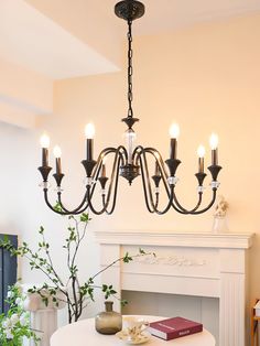 a chandelier hanging over a white table in a room with a fireplace and potted plant