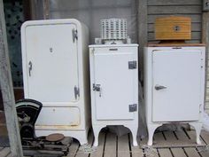 three old white refrigerators sitting next to each other on a wooden floor in front of a building