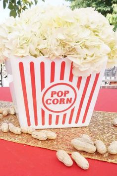 a popcorn box with flowers in it sitting on a red cloth covered tablecloth next to peanuts