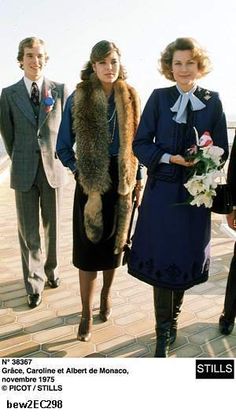 three women and two men are standing on a pier with flowers in their hands, one is wearing a fur stole