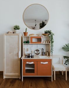 a small wooden play kitchen with an oval mirror on the wall and potted plants next to it