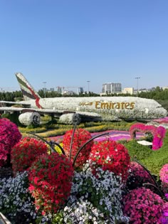 a large jetliner sitting on top of a lush green field next to flowers and trees