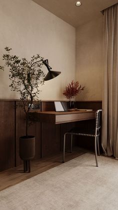 a room with a desk, chair and potted plant on it in front of a window