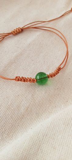 a green beaded bracelet with an orange cord on a white cloth tablecloth background