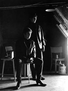 black and white photograph of two men sitting on chairs in a dark room with light coming from the ceiling