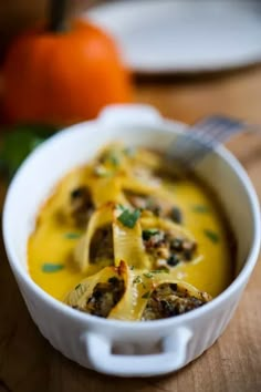 a white bowl filled with food on top of a wooden table next to an orange pumpkin