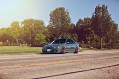 the car is parked on the side of the road in front of some trees and grass