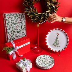 a table topped with plates and gifts next to a christmas tree wreath on top of a red wall