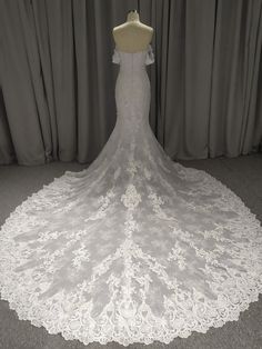 a white wedding dress on display in front of a gray curtain with the back of it's lace