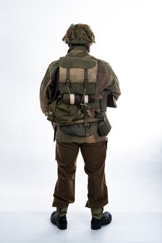 the back view of a man wearing an army jacket and pants, standing in front of a white background