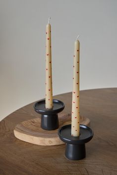 two candles sitting on top of each other in front of a wooden table with black bases