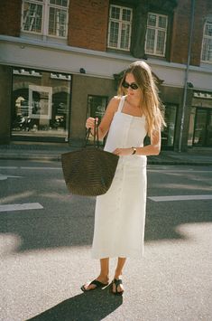 a woman is standing on the street holding a straw bag