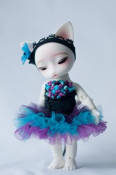 a white cat doll wearing a purple and blue tutu with flowers in her hair