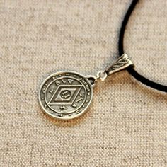 a necklace with a medallion on it sitting on top of a piece of cloth next to a black cord