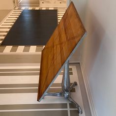 a wooden table sitting on top of a metal stand next to a white and gray wall