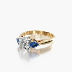 a diamond and blue sapphire engagement ring on a white background, with the center stone in yellow gold