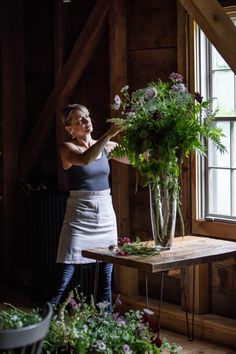 a woman arranging flowers in a vase on a table