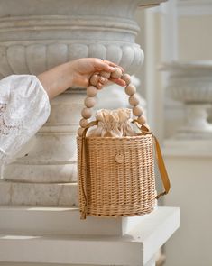 a person holding a wicker bag with beads on it's handle, sitting next to a statue