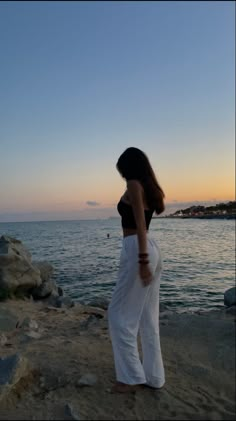 a woman standing on top of a sandy beach next to the ocean at sunset or dawn